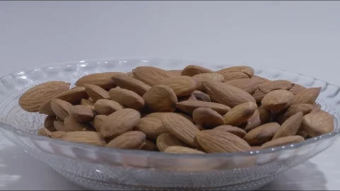 Close up static shot of unshelled almonds falling into empty plate on table Stock Footage 280337551