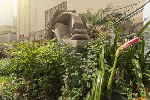 Close-up on a statue of a Moai head surrounded by tropical flowers in Shibuya Foto stock