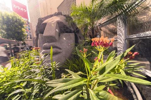 Close-up on a statue of a Moai head surrounded by tropical flowers at the ... Foto stock