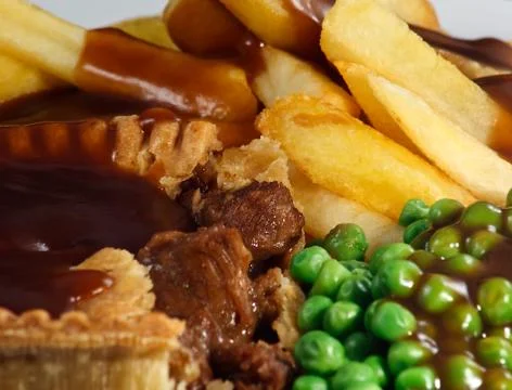 Close up of steak pie and chips with peas and gravy. Stock Photos