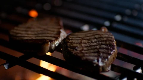 Close up of steaks on restaurant grill with fire flames, chef turns them over Stock Footage 92698841