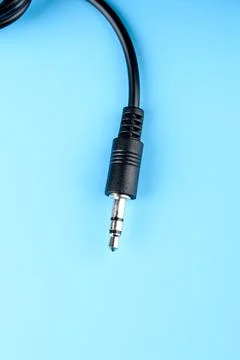 A close-up of a stereo jack on a black wire against a blue background. Stock Photos