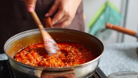 Close-up of stirring red tomato meat sauce with wooden spatula in pan on stove Stock Footage 345376726
