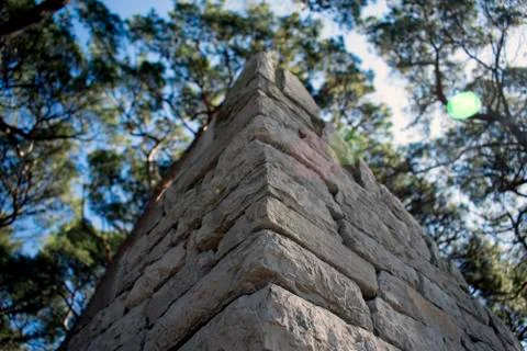 Close up of a stone wall corner, with trees an sky in background Stock Photos