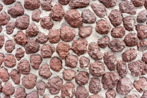 Close up of stone wall texture made from irregular red volcanic rocks set in  Фото