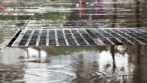 Close up of Storm Drain Grate Side View and Flooded Pavement with Rain drops Stock Footage 343907078