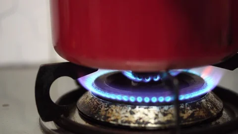 Close up Stove top burner igniting into a blue cooking flame heating metal pot. Stock Footage 121108622