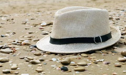Close up of straw hat on a sandy and grey stone beach.  Summer time vacation. Stock Photos