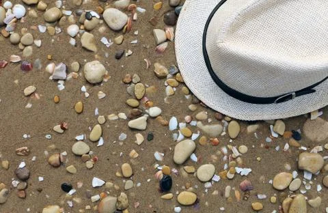 Close up of straw hat on a sandy and grey stone beach.  Summer time vacation. Stock Photos