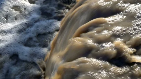 Close-up of a stream of dirty, muddy water that falls into the river  Stock Footage 104663223