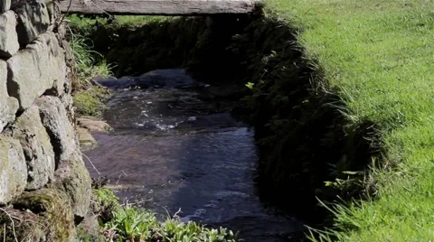 Close Up Stream Water Flows Past Grass Bank and Old Stone Wall 動画素材 49069920