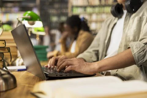 Close-up of student hands typing on laptop at wooden library table Stock Photos
