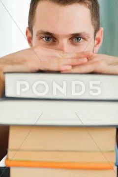 Close up of student hiding behind a pile of books Stock Photos