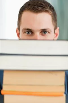 Close up of student hiding behind a stack of books Foto stock