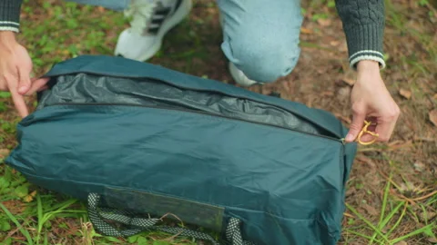 Close up of student pulling tent bag from zipped case on grassy forest ground Video stock 310472660