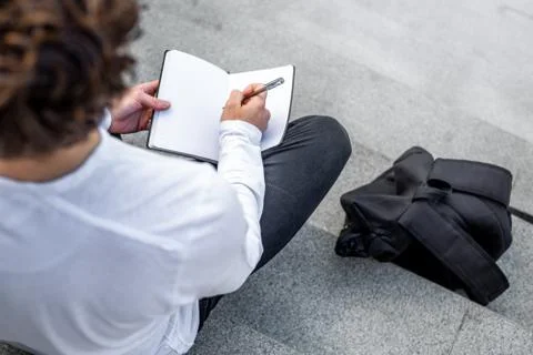Close up of student on steps of modern building and writing text in notepad. Foto stock