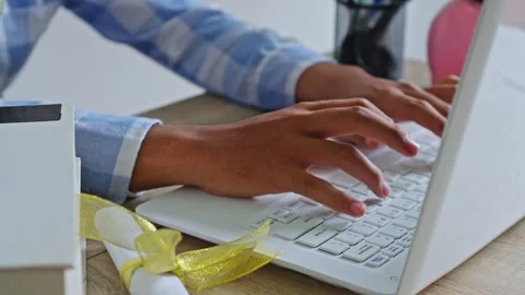 Close-up of student typing on laptop with diploma and books on desk Stock Footage 333940492