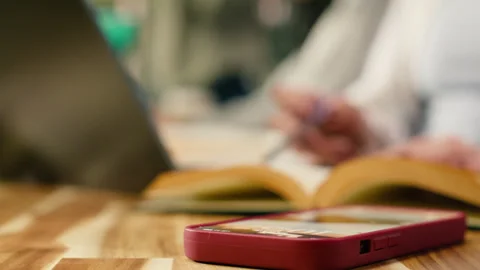 Close up of student using laptop at desk and receives phone message Stock Footage 336360609