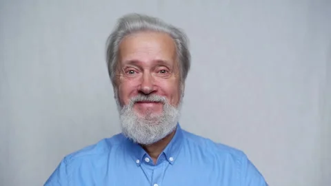 Close-up studio portrait of cheerful gray-haired mature man smiling looking at Video stock 169021233