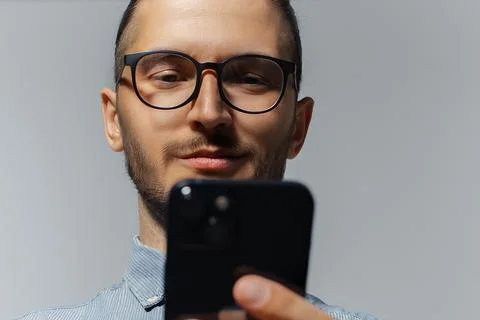 Close-up studio portrait of smiling guy looking in smartphone, wearing eyegla Stock Photos