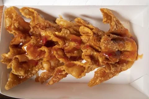 A close-up studio shot of a batch of crispy fried wontons drizzled with swe.. 스톡 사진
