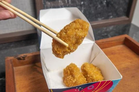 A close-up studio shot of a breaded fried snack being held by wooden chopst.. Фото