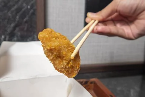 A close-up studio shot of a breaded fried snack being held by wooden chopst.. Fotos Stock