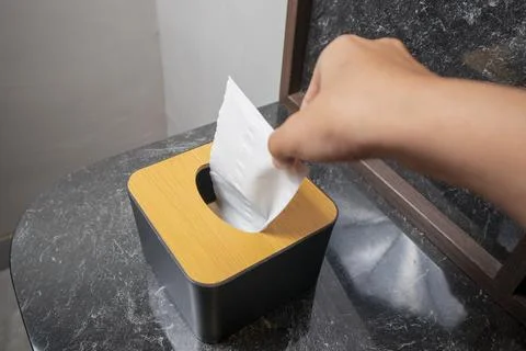 A close-up studio shot of a hand pulling a tissue from a black and wood tis.. 写真素材
