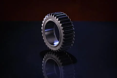 A close-up studio shot of a large, metallic gear resting on a dark, reflective Foto stock