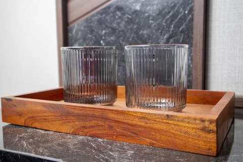 A close-up studio shot of two ribbed glass tumblers resting on a wooden tra.. Stock-Fotos