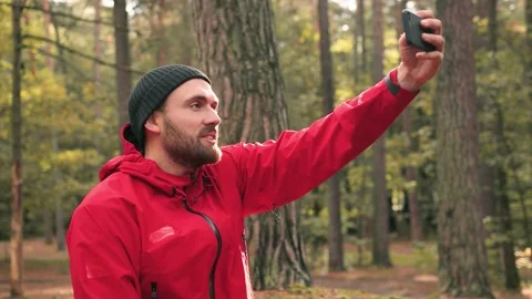 Close up of stylish man in hat and red jacket sitting in woods and makes photo Stock Footage 147066175