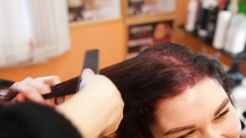 Close up of stylist using flat iron on  hair of female client in salon Stock Footage 101299002