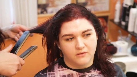 Close up of stylist using flat iron on  hair of female client in salon Stock Footage 101348511