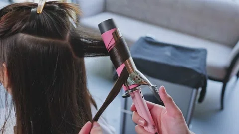 Close up of stylist's hand use curling iron make curly to woman in beauty salon. Video stock 167844468