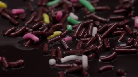 Close-up of sugared colored sprinkles falling on a chocolate candy Stock Footage 304114317