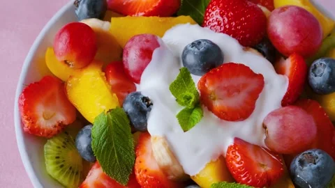 Close up of summer colorful fruit salad with creamy yogurt in a bowl on pink Stock Footage 315860675