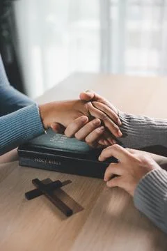 Close up of supportive hands over a Holy Bible with a wooden cross on the t.. Stock Photos