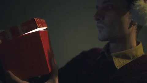 Close up of surprised man opening luminous gift box at night Christmas Eve time Stock Footage 70190872