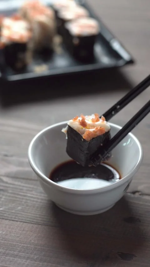 Close up sushi roll dipped in soy sauce with chopsticks on rustic wooden tabl Video stock 335424436