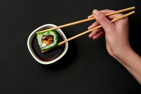 Close-up on a sushi roll with eel and cucumber dipped in soy sauce. Dark back Stock Photos