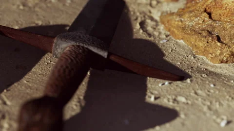 Close up of a sword resting on the ground near a rock in natural light Stock Footage 340212425