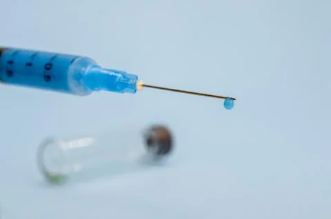A close-up syringe needle with a drop of solution at the end against an empty Foto stock