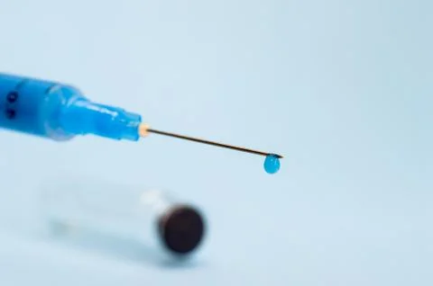 A close-up syringe needle with a drop of solution at the end against an empty Stock Photos