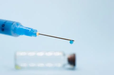 A close-up syringe needle with a drop of solution at the end against an empty Stock Photos