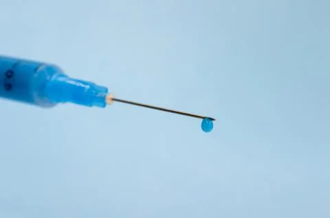Close-up of a syringe needle with a drop of solution at the end on a blue Stock Photos