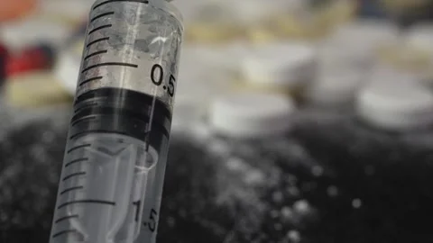 Close-up syringe plunger with blurred background of pills and medicines Stock Footage 263744314
