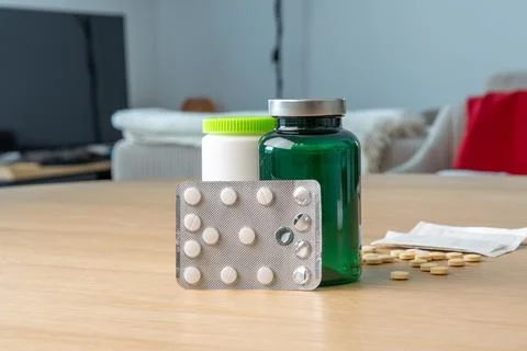 A close-up of a table with a blister pack of pills, a green bottle, and scatt Stock Photos