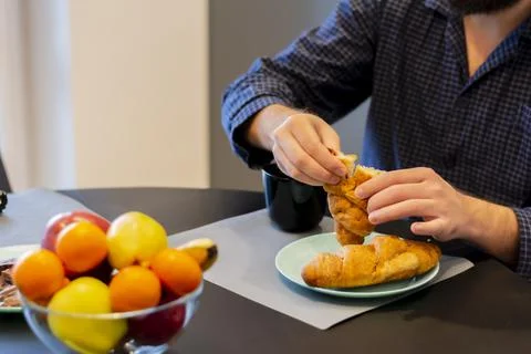 Close-up table hands of a young man eating a delicious fragrant croissant for Stock Photos