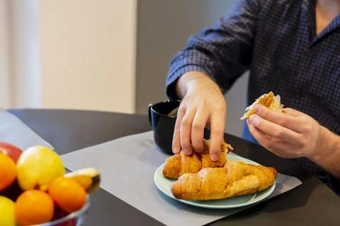 Close-up table hands of a young man eating delicious fragrant croissant diet Stock Photos