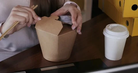 Close-up of table in office, girl types on laptop, reaches for box of noodles Stock Footage 130367449